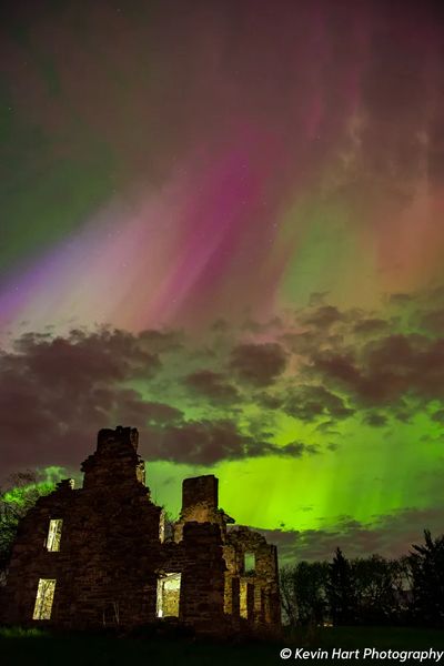 Streaks of magenta and green stream up from an abandoned building.